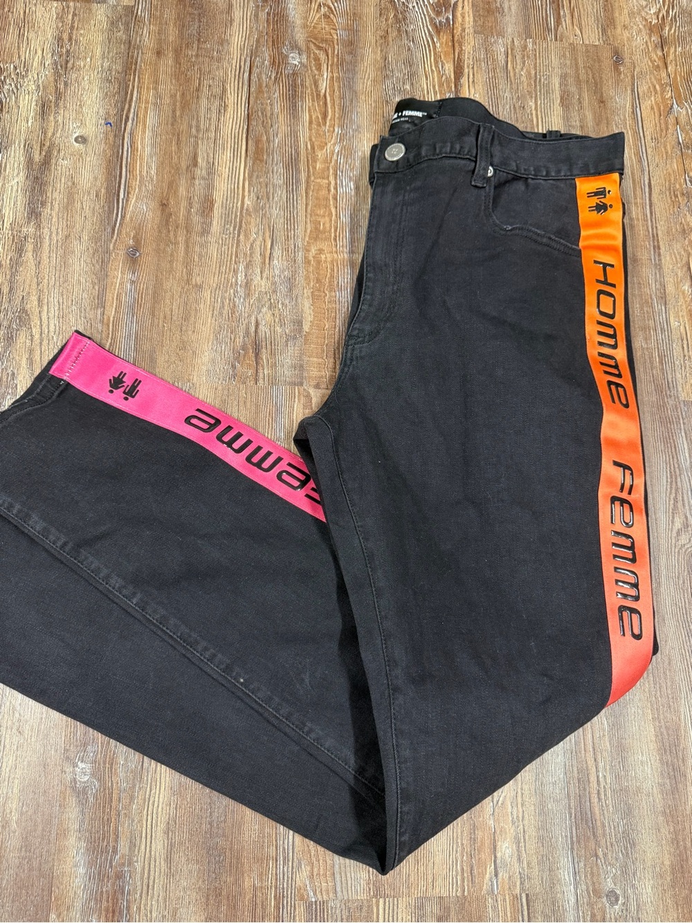 Femme Homme black jeans with orange and pink side stripes featuring repeating 'H
